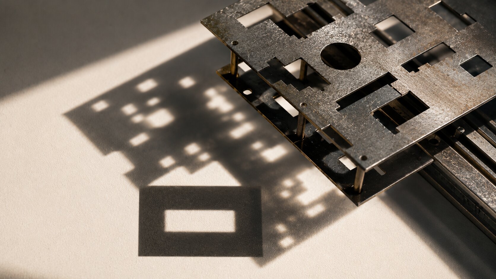 Layered metal plates align under directional light to create one bold readable shadow, representing controlled thumbnail testing and visual simplification.