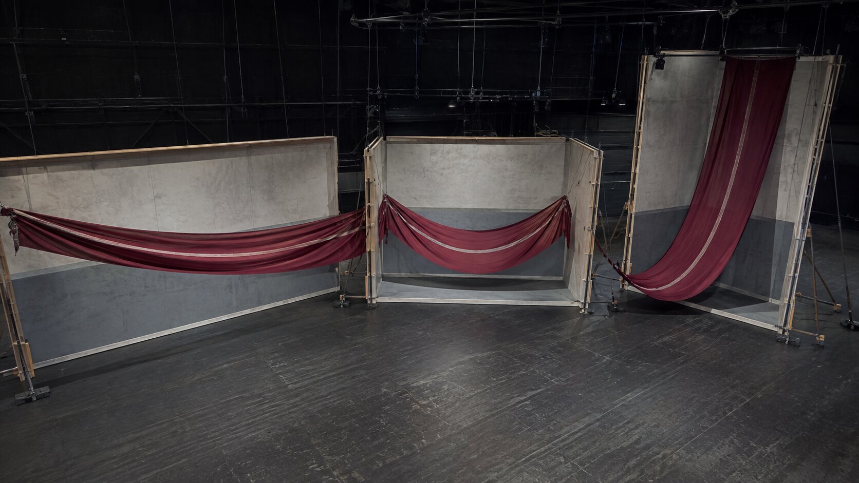 An empty production stage uses three differently proportioned set bays to reshape one continuous burgundy canvas ribbon while keeping its defining pale seam visible.