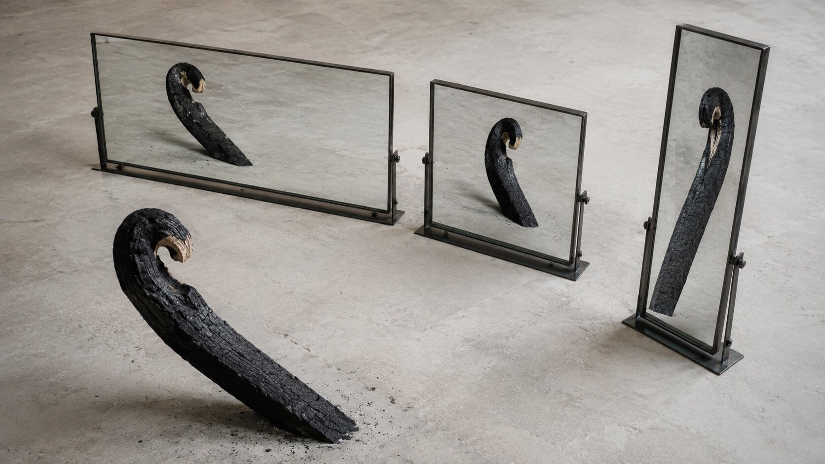 A hooked charred-wood form remains recognizable in three differently proportioned mirrors, representing creative identity preserved through deliberate recomposition for each publishing format.